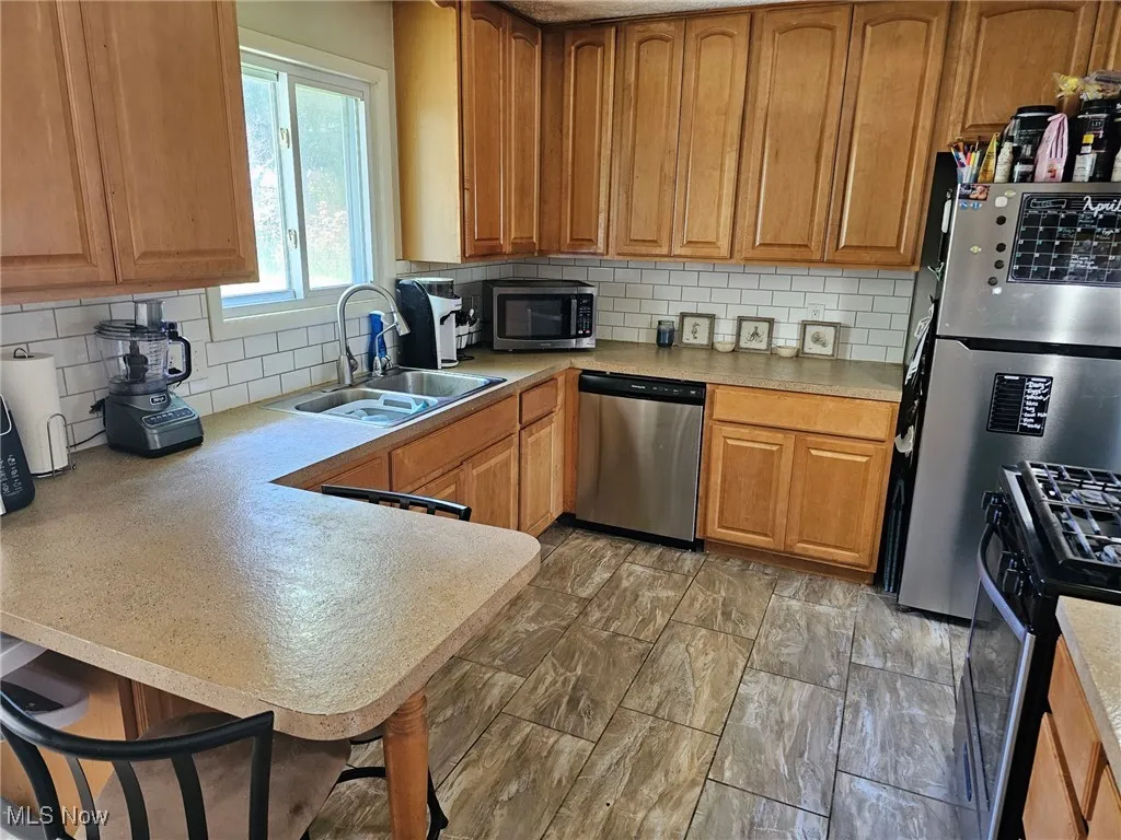 Kitchen featuring decorative backsplash, a sink, light countertops, a peninsula, and stainless steel appliances