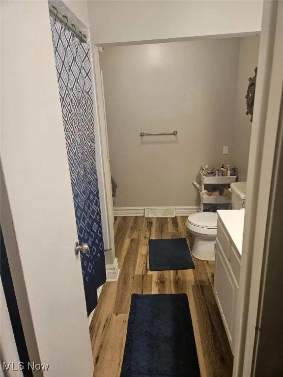 Full bath with toilet, a shower with curtain, wood finished floors, and vanity