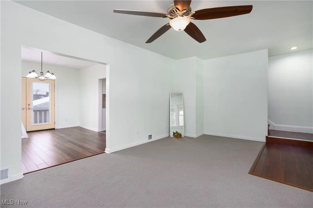 Unfurnished living room with baseboards, ceiling fan with notable chandelier, and carpet floors