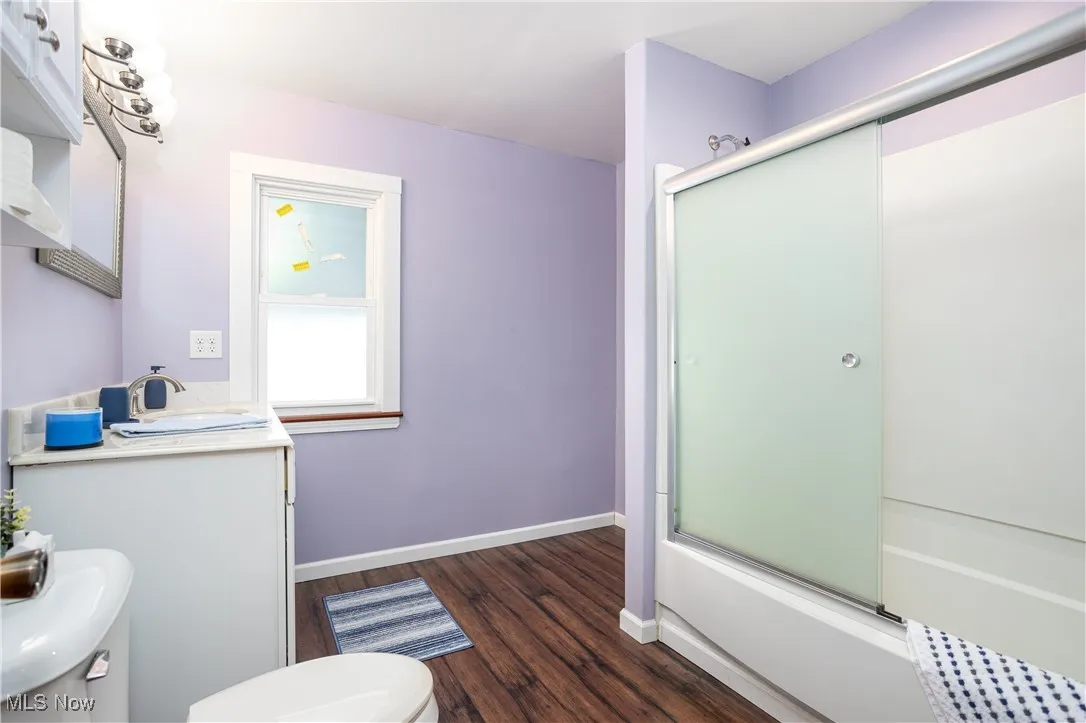 Full bath featuring vanity, bath / shower combo with glass door, toilet, baseboards, and wood finished floors