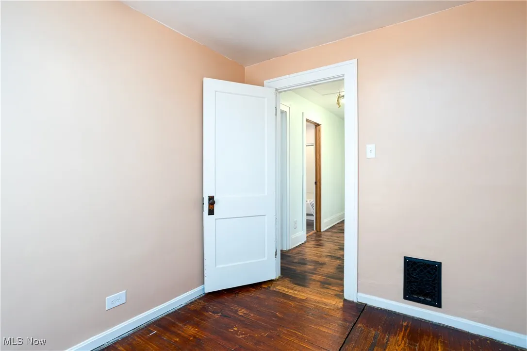 Empty room featuring visible vents, dark wood finished floors, and baseboards