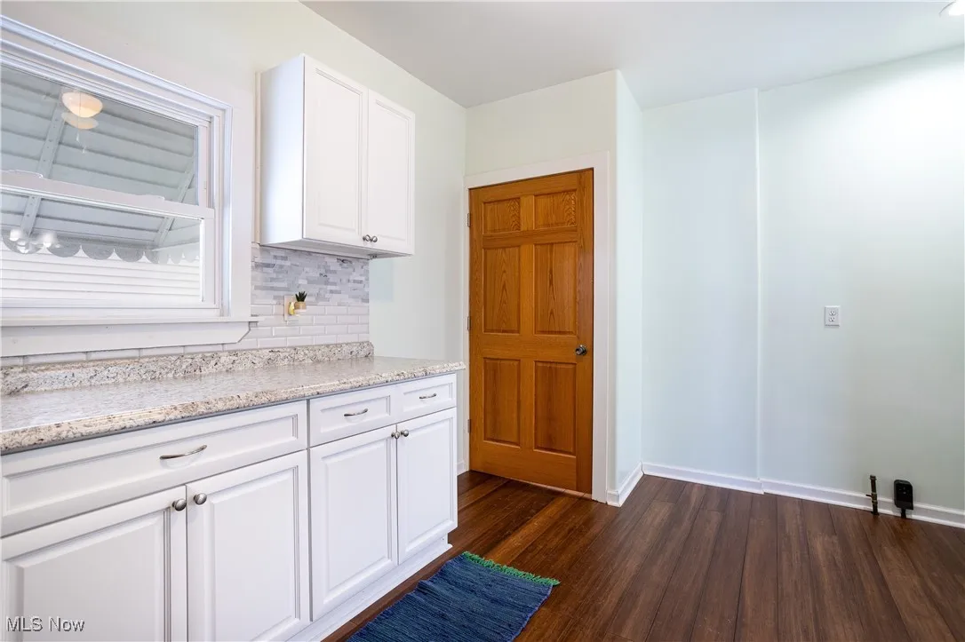 Kitchen with light stone counters, tasteful backsplash, white cabinets, baseboards, and dark wood-type flooring