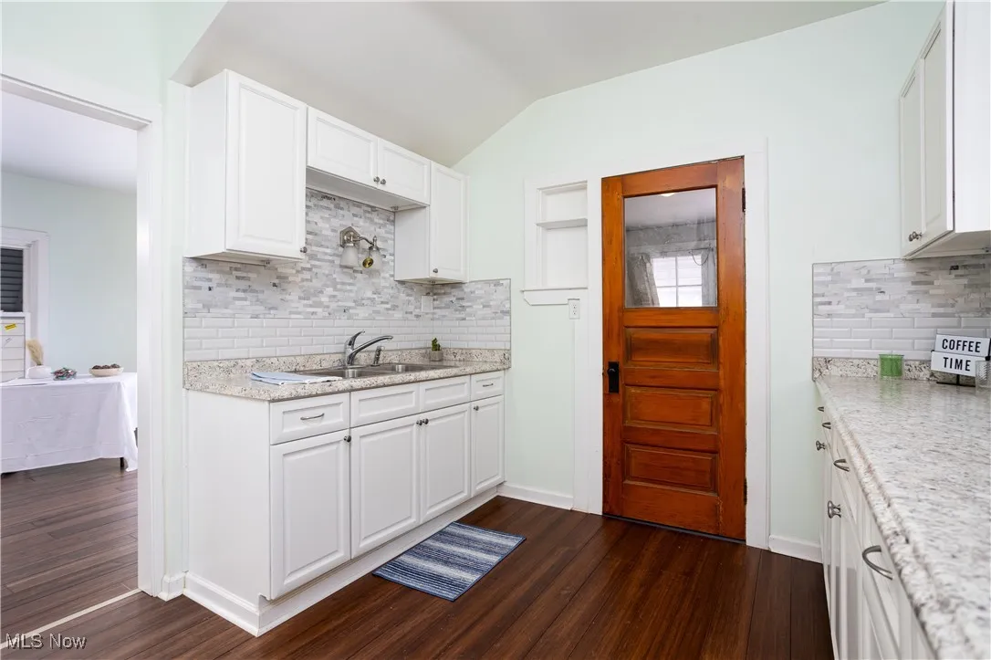 Kitchen with a sink, white cabinets, dark wood-style flooring, and tasteful backsplash