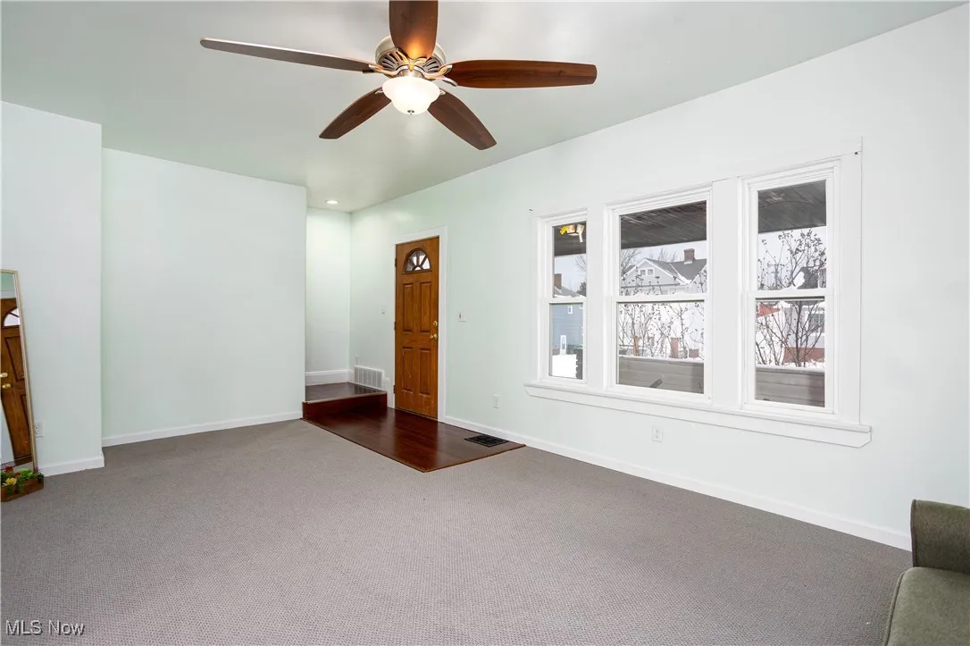 Unfurnished living room with visible vents, dark colored carpet, ceiling fan, and baseboards
