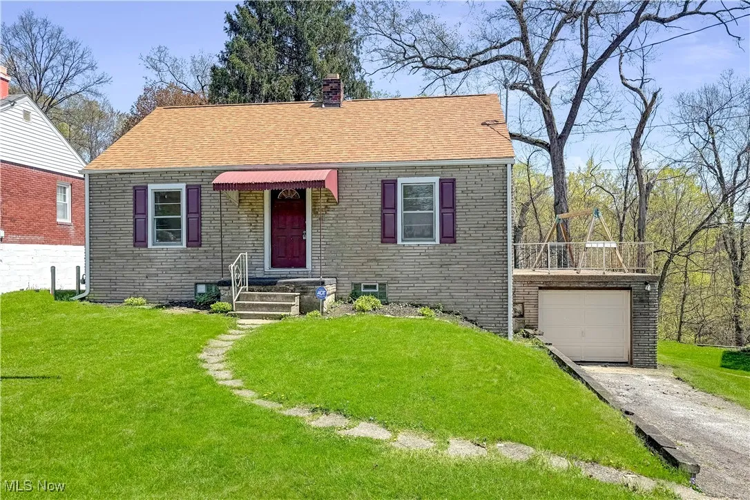 Bungalow with a front yard, brick siding, a chimney, roof with shingles, and concrete driveway