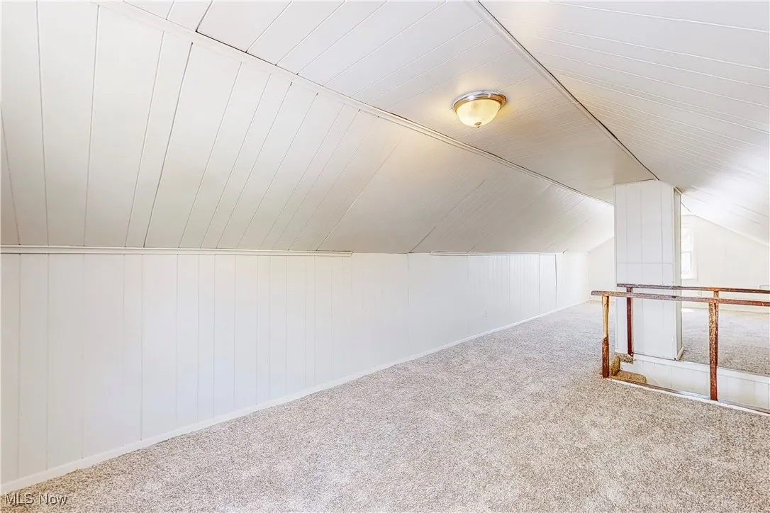 Additional living space with lofted ceiling, wood walls, and carpet flooring