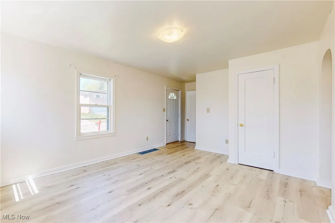 Spare room featuring baseboards, visible vents, arched walkways, and light wood finished floors