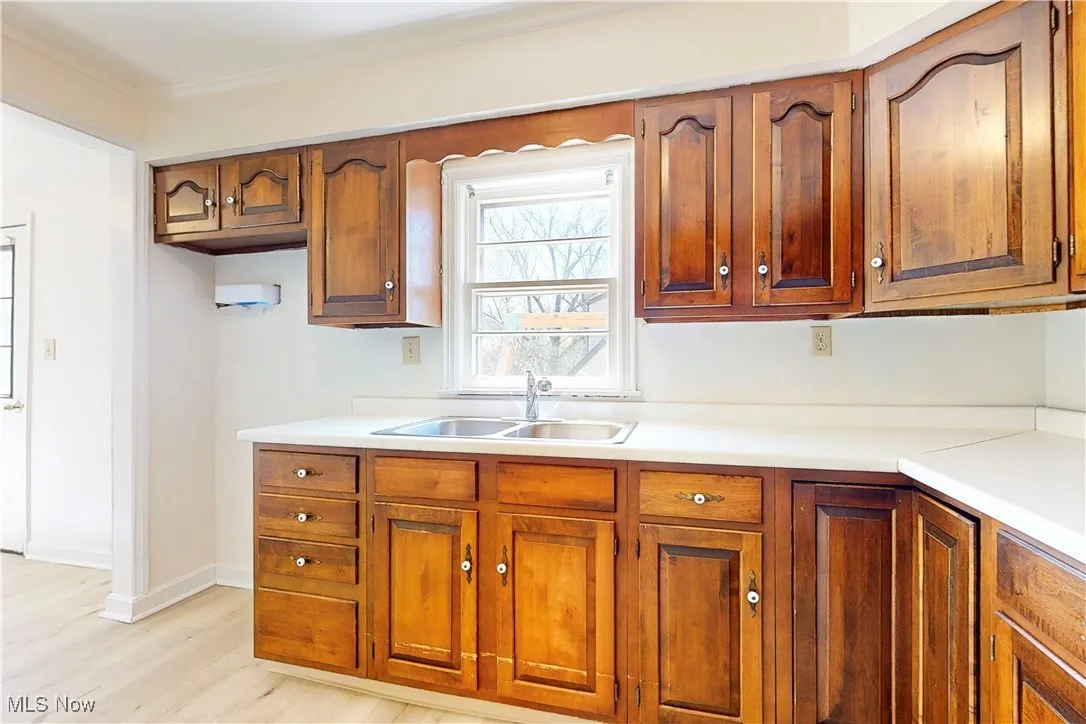 Kitchen with a sink, brown cabinets, crown molding, light wood-style flooring, and light countertops