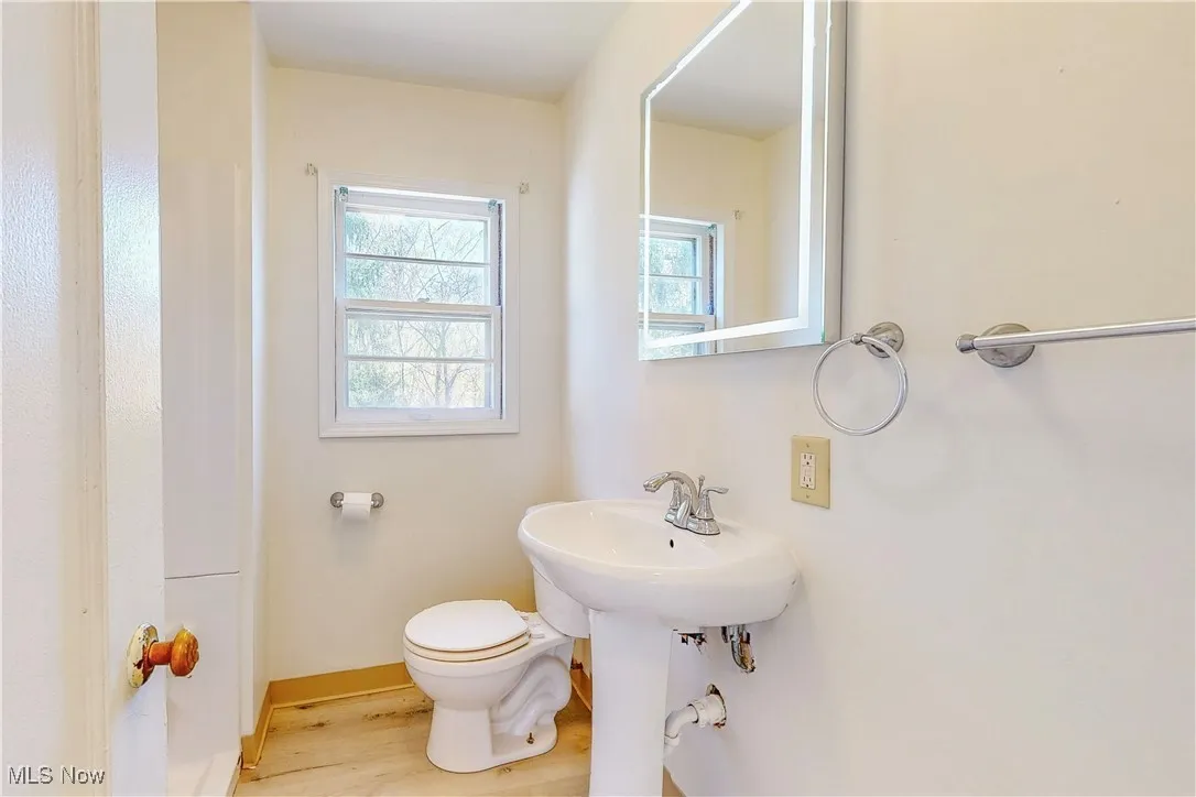 Half bathroom featuring wood finished floors, toilet, and baseboards