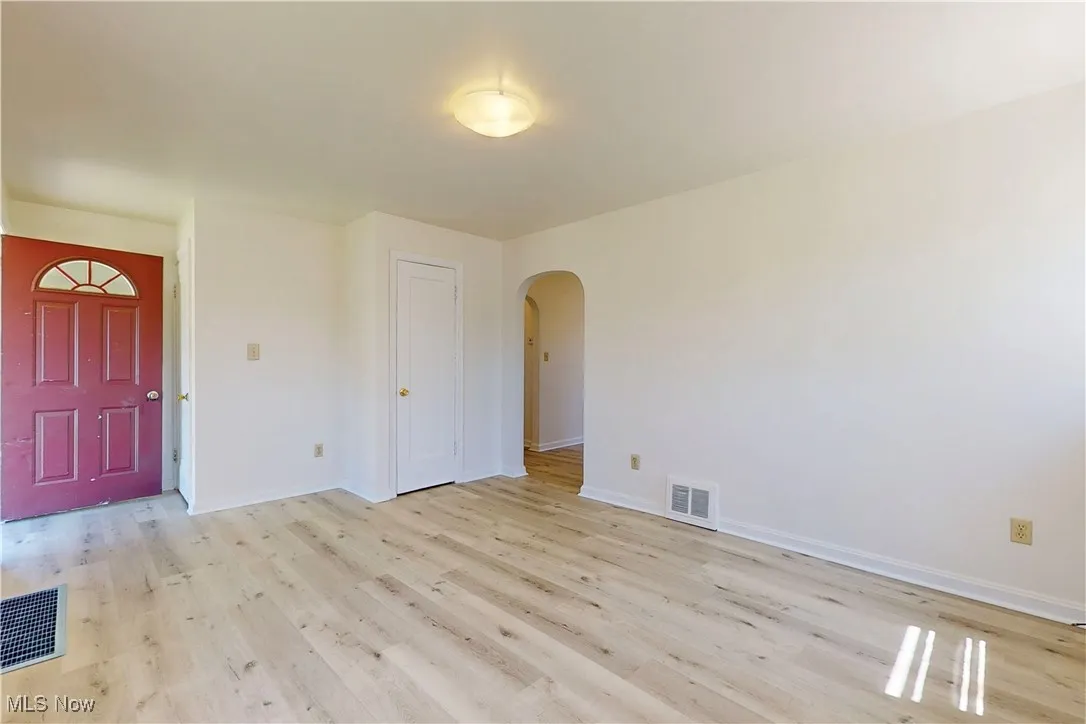 Foyer entrance with visible vents, baseboards, light wood finished floors, and arched walkways