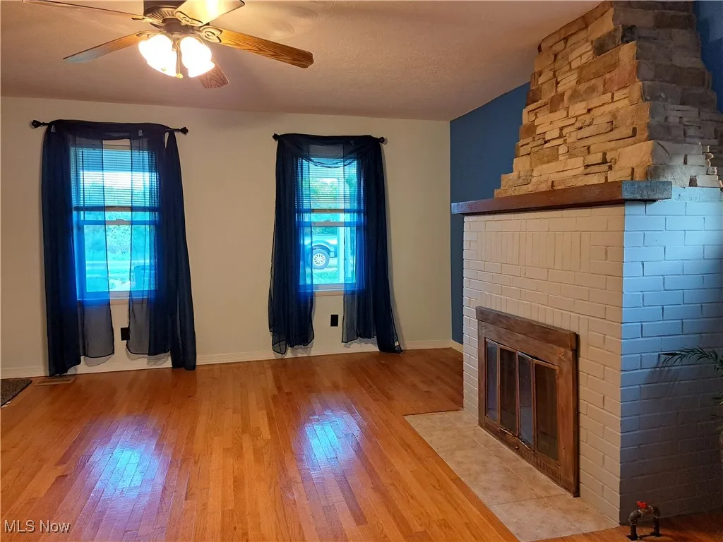 Unfurnished living room with ceiling fan, a fireplace, and light hardwood / wood-style flooring