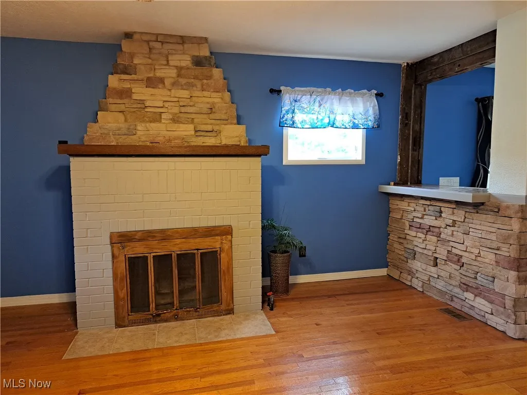 Unfurnished living room with wood-type flooring and a stone fireplace