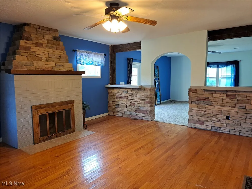Unfurnished living room featuring a stone fireplace, ceiling fan, light hardwood / wood-style flooring