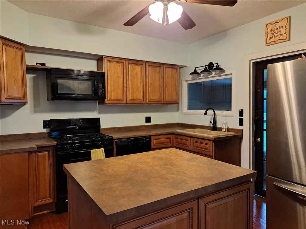 Kitchen featuring black appliances, sink, a kitchen island, dark wood-type flooring, and ceiling fan