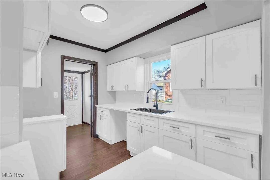 Kitchen with light countertops, a sink, white cabinetry, and dark wood-type flooring
