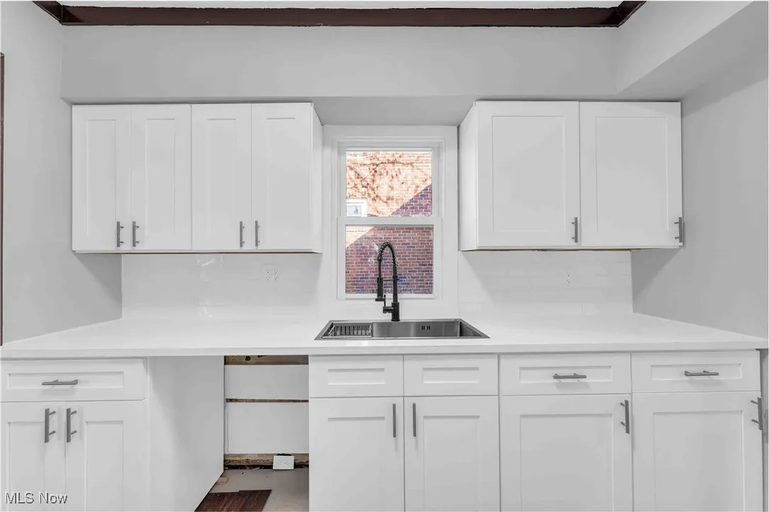 Kitchen with tasteful backsplash, light countertops, white cabinets, and a sink
