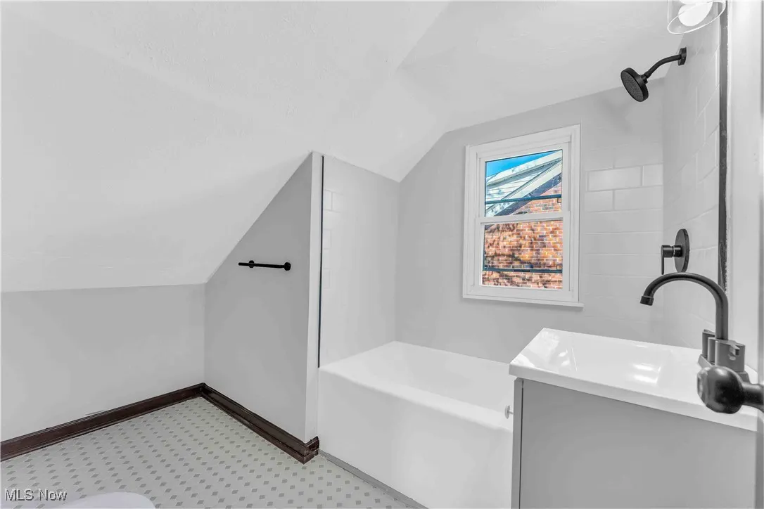 Bathroom featuring walk in shower, a bathing tub, a sink, baseboards, and lofted ceiling