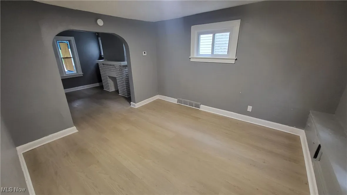 Empty room with arched walkways, light wood-style flooring, and baseboards