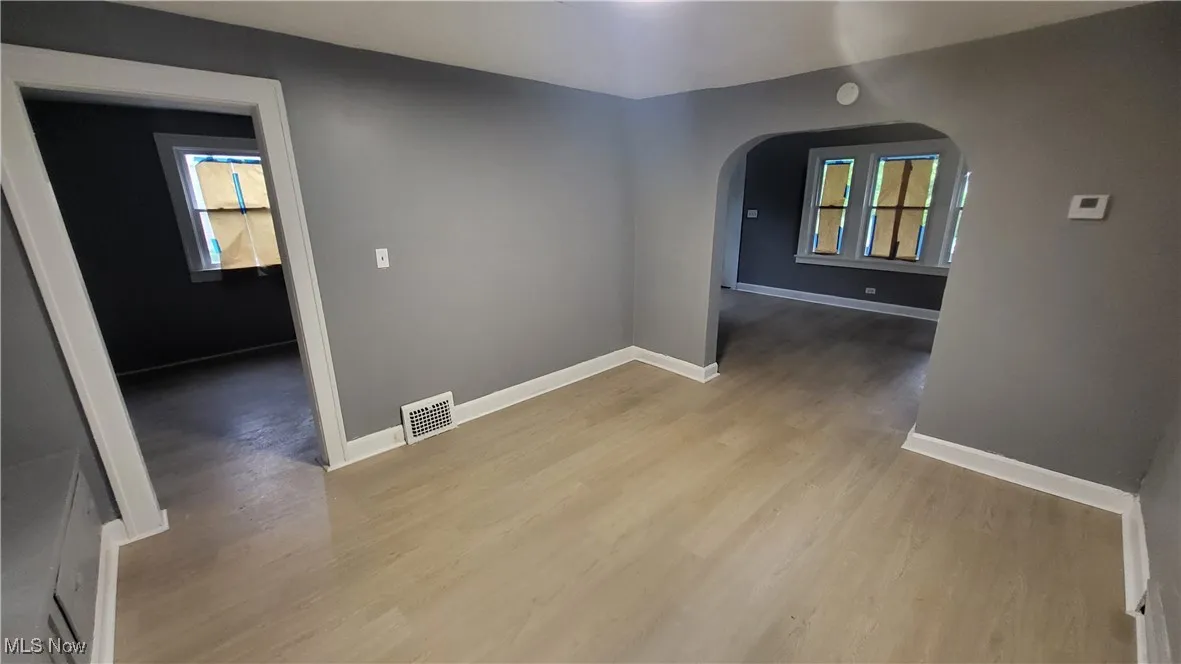 Unfurnished room with arched walkways, wood finished floors, baseboards, and a smoke detector