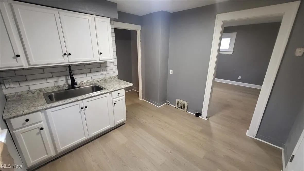 Kitchen with a sink, light wood-style flooring, baseboards, and white cabinetry