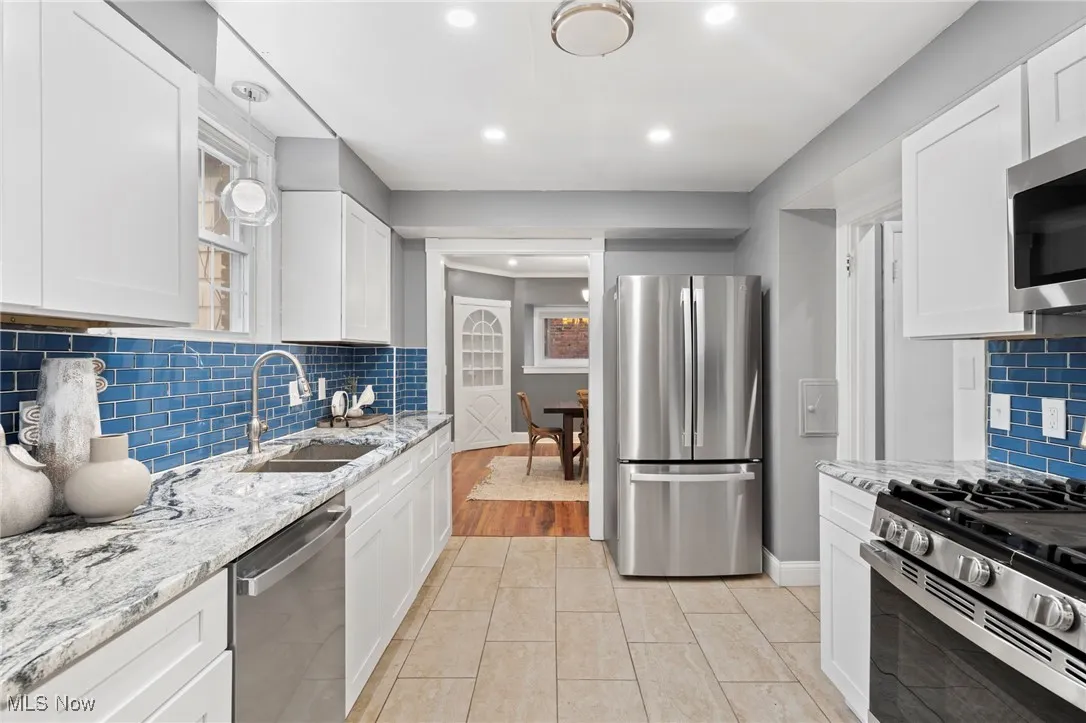 Kitchen with decorative backsplash, stainless steel appliances, sink, light stone countertops, and white cabinetry