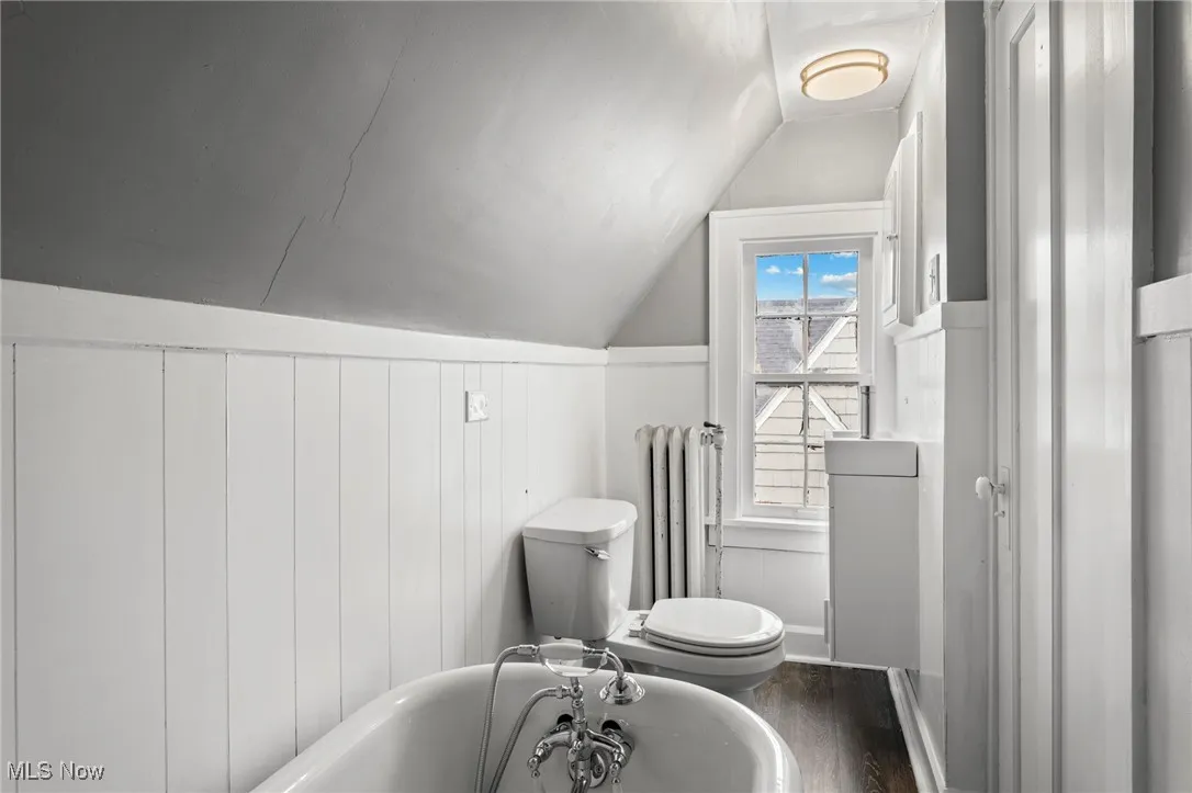 Bathroom with a bathing tub, lofted ceiling, radiator heating unit, wood-type flooring, and toilet