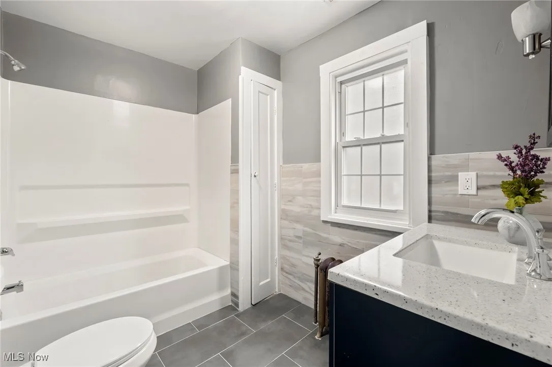 Full bathroom with vanity, tile walls, toilet, and tub / shower combination