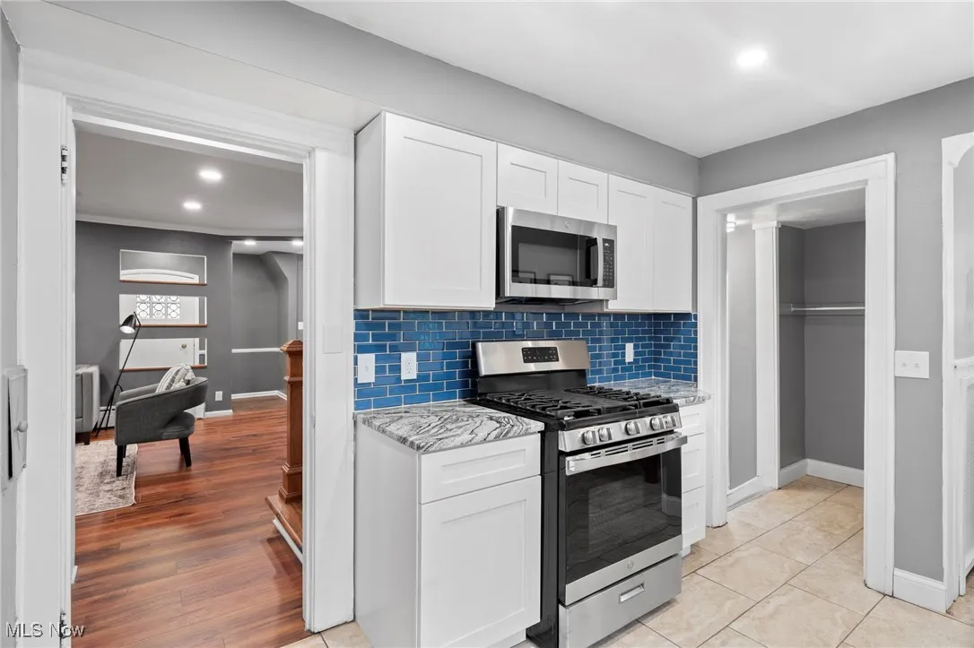 Kitchen with decorative backsplash, white cabinets, appliances with stainless steel finishes, light stone counters, and light hardwood / wood-style floors