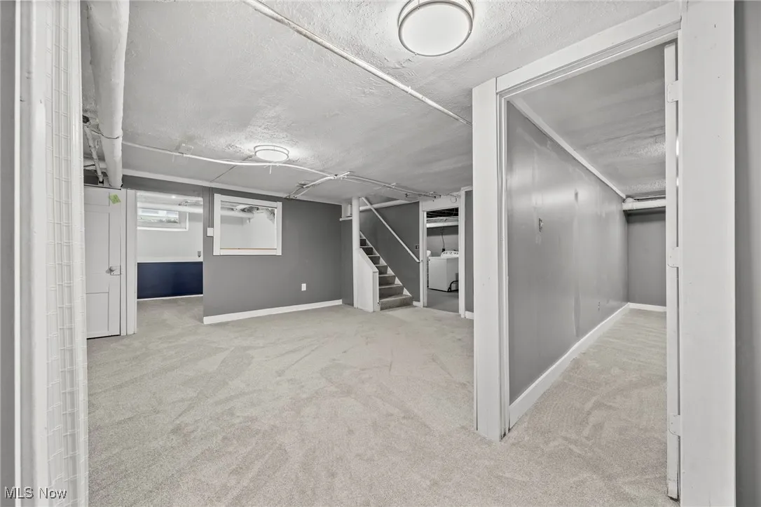 Basement with light carpet, a textured ceiling, and washer / clothes dryer