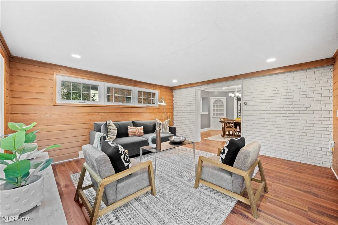 Living room featuring wooden walls, hardwood / wood-style flooring, a chandelier, and brick wall