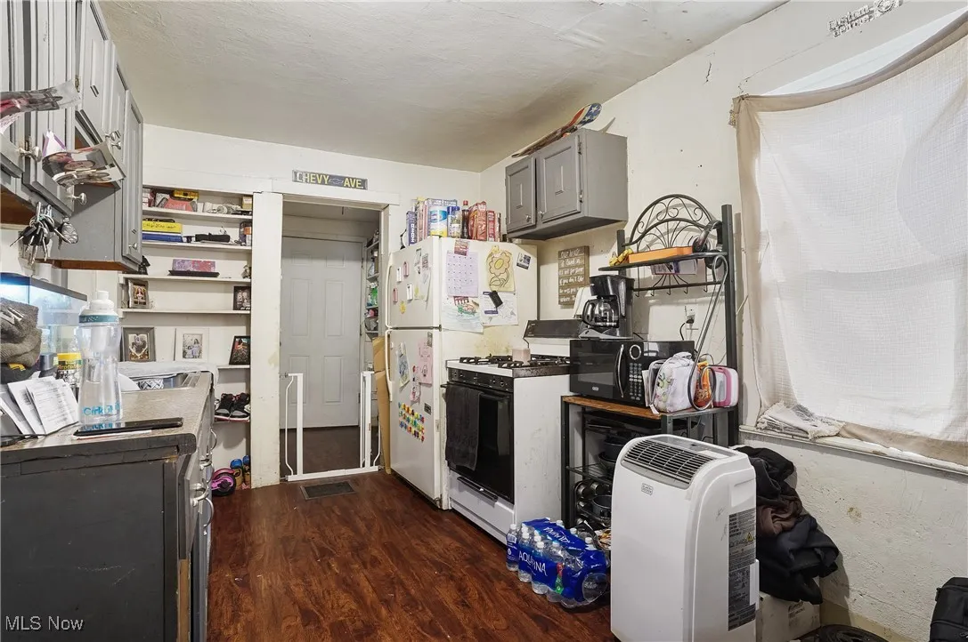 Kitchen with white range with gas stovetop, black microwave, dark wood-style flooring, and gray cabinets
