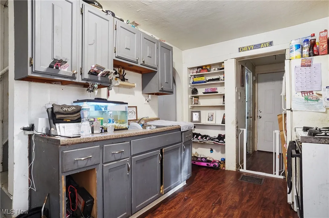 Kitchen with gas stove, open shelves, gray cabinets, and dark wood-style flooring