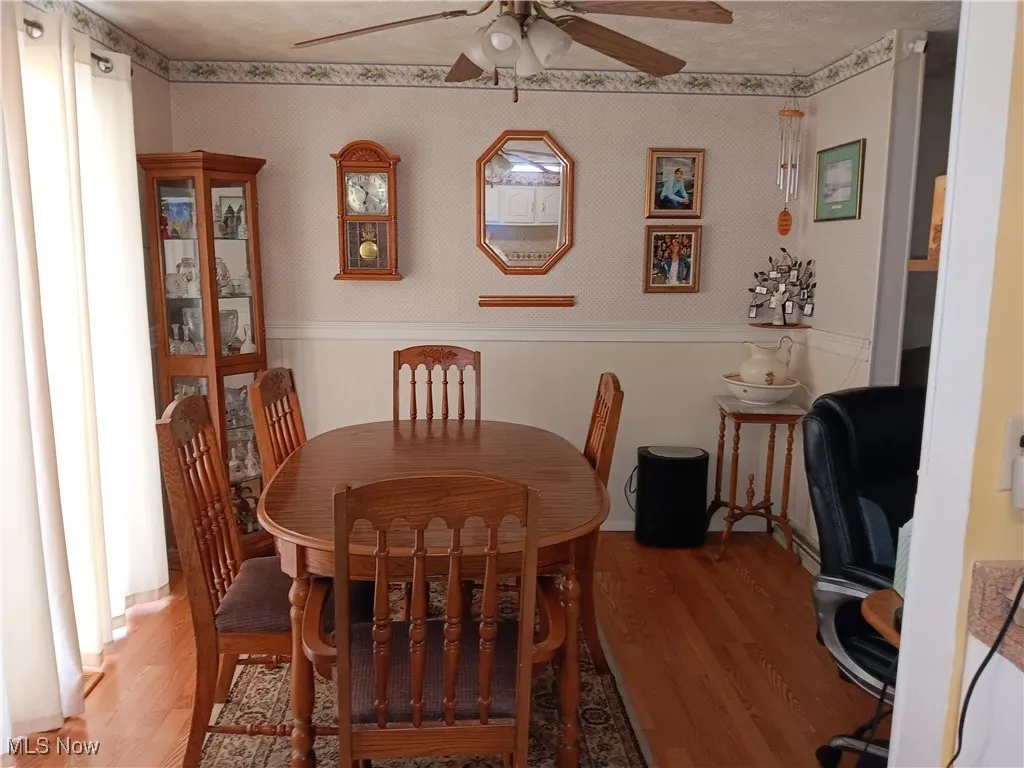 Dining space with ceiling fan, light wood finished floors, and a wainscoted wall