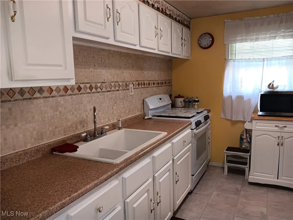 Kitchen with backsplash, a sink, stainless steel microwave, electric stove, and white cabinetry