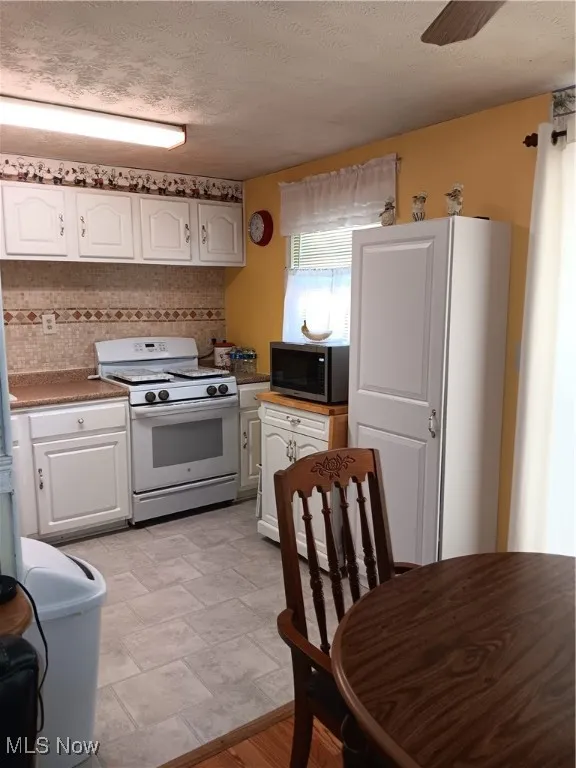 Kitchen featuring a textured ceiling, tasteful backsplash, stove, white cabinets, and stainless steel microwave