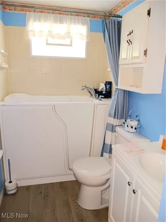 Full bathroom featuring a bath, wood finished floors, vanity, toilet, and a shower with shower curtain