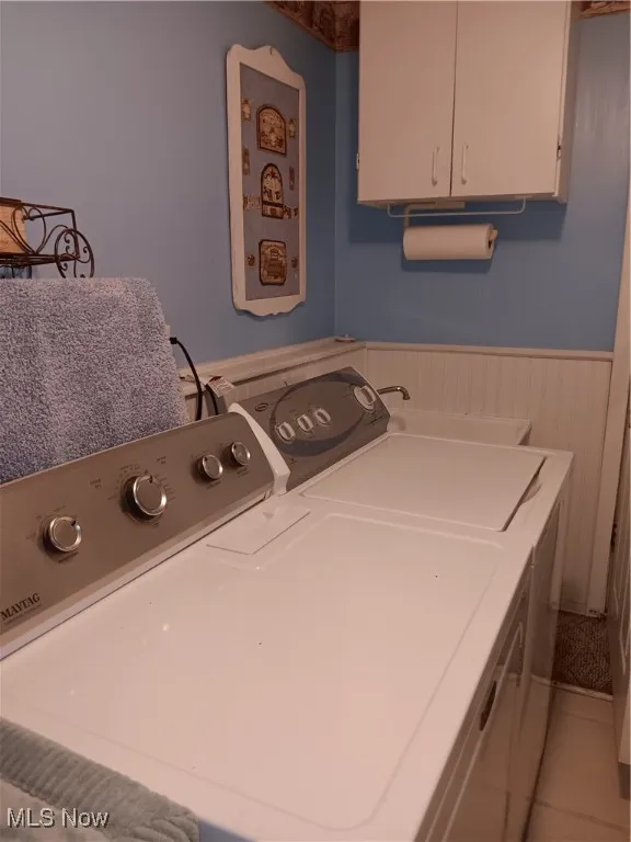 Laundry area featuring wainscoting, light tile patterned floors, washing machine and dryer, and cabinet space