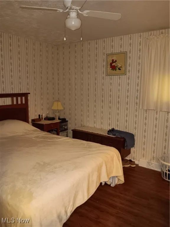 Bedroom featuring baseboards, a ceiling fan, dark wood-style floors, and wallpapered walls