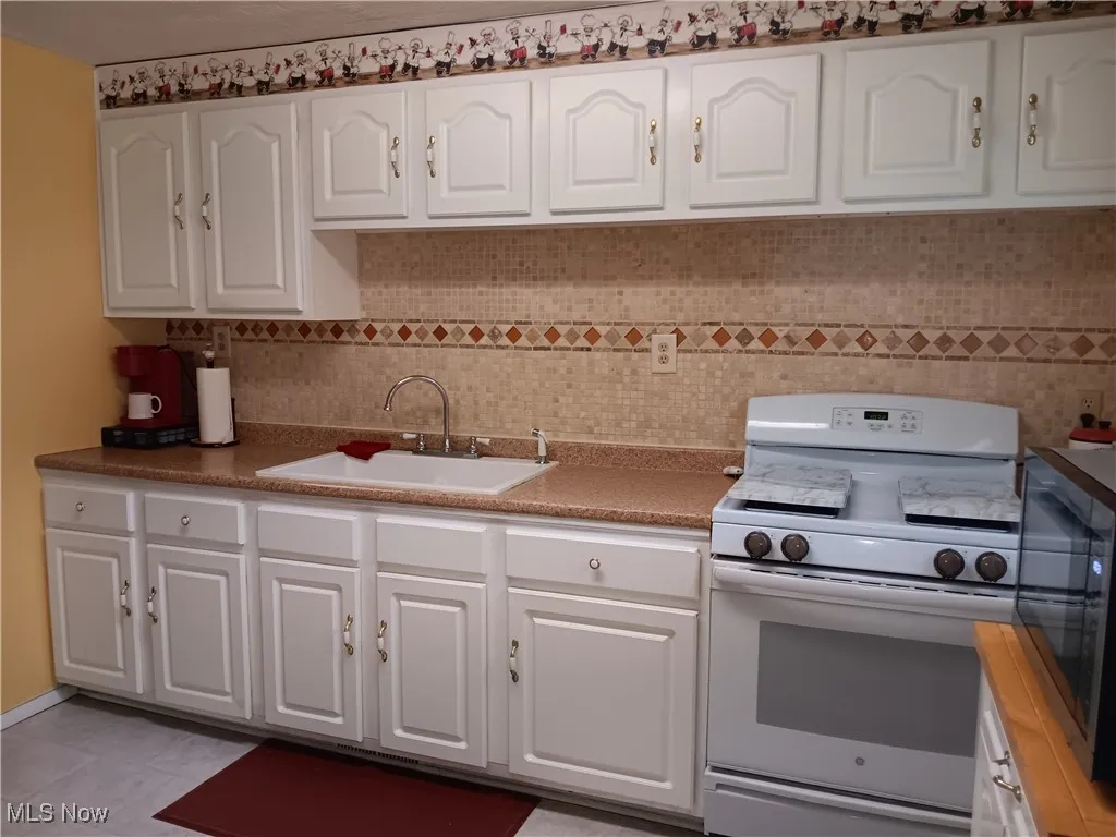 Kitchen featuring black microwave, tasteful backsplash, a sink, white range with gas cooktop, and white cabinetry