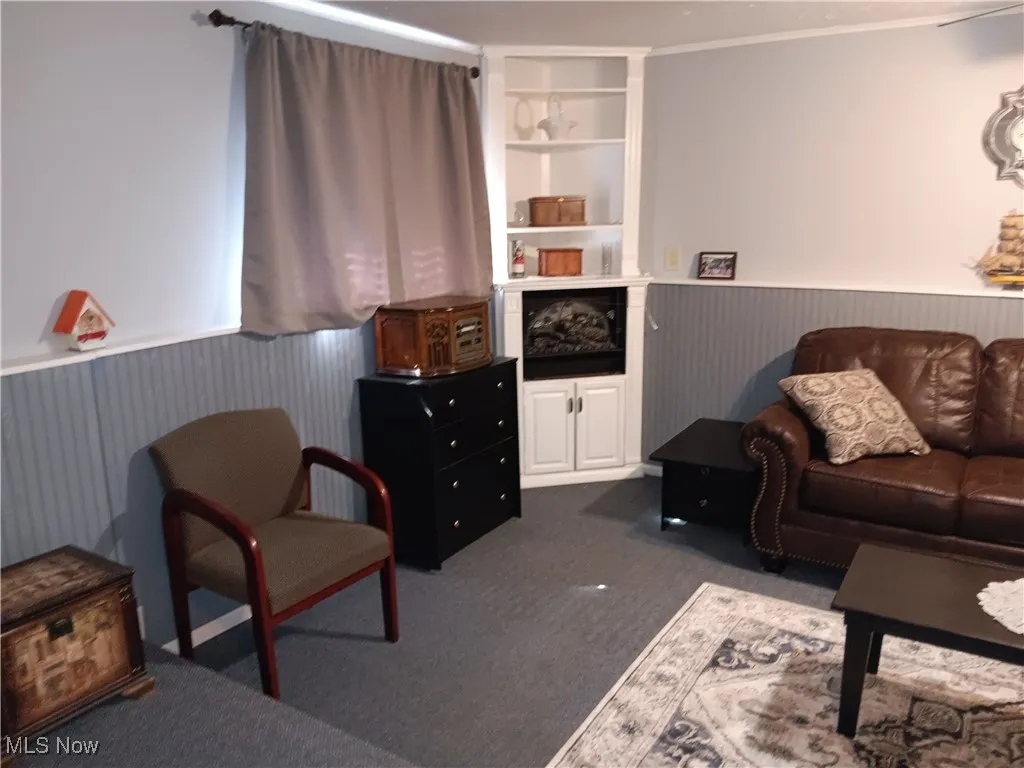 Living area with dark carpet, ornamental molding, wainscoting, and built in features