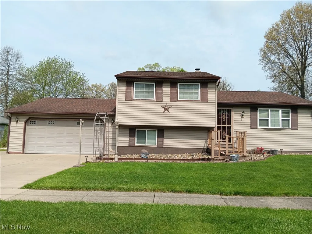 Tri-level home with central air condition unit, an attached garage, concrete driveway, and a front yard