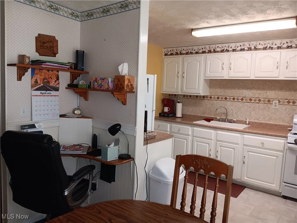 Kitchen featuring white cabinets, wallpapered walls, a sink, and open shelves