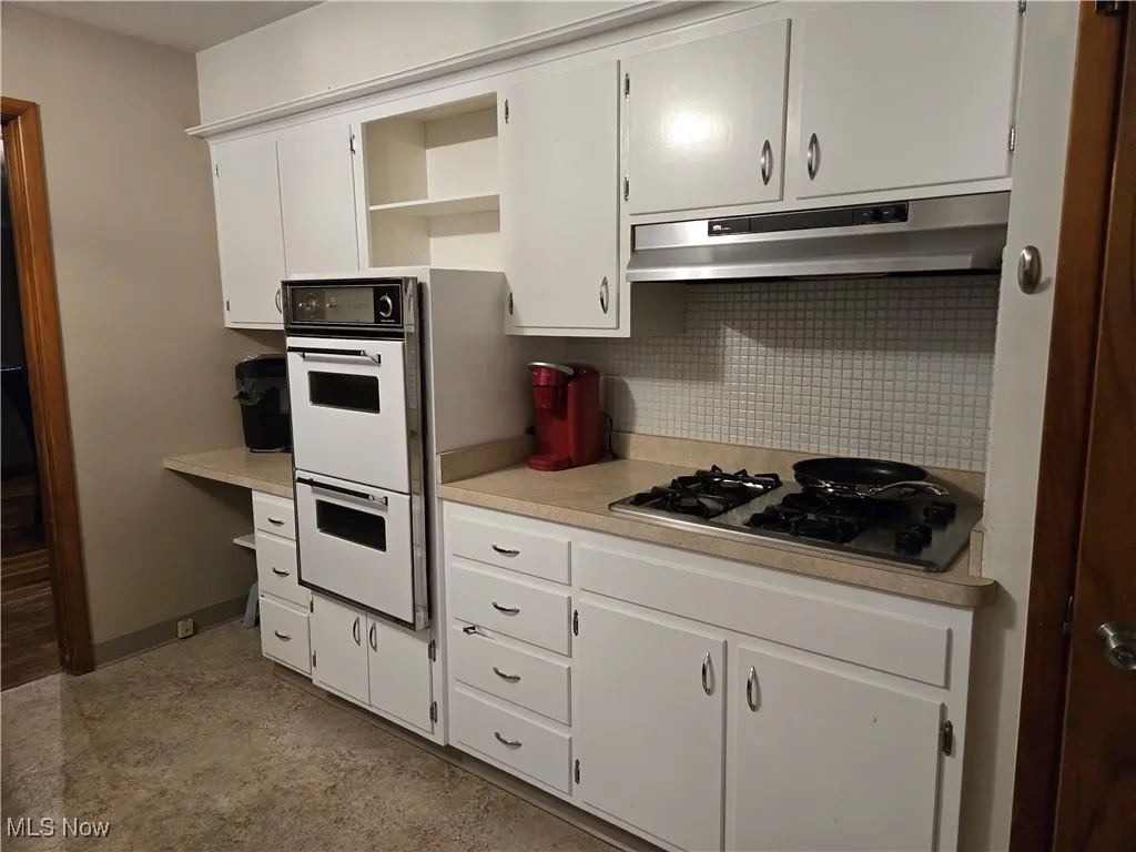 Kitchen featuring open shelves, double oven, light countertops, stainless steel gas cooktop, and under cabinet range hood