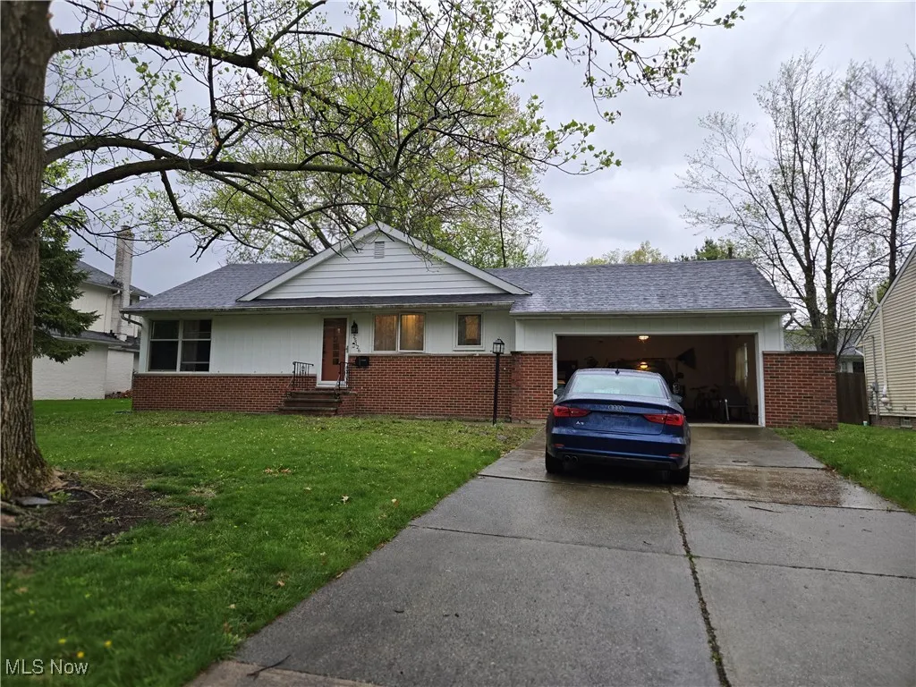 Single story home featuring roof with shingles, an attached garage, brick siding, a front yard, and driveway
