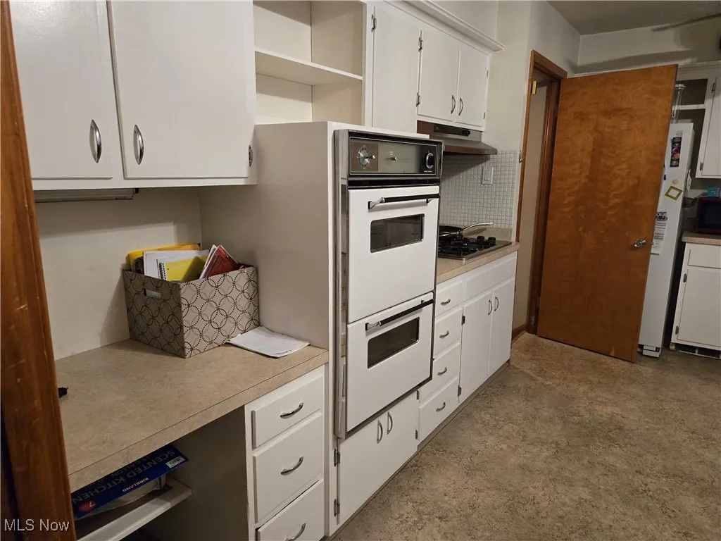 Kitchen featuring light countertops, white cabinets, under cabinet range hood, and white appliances