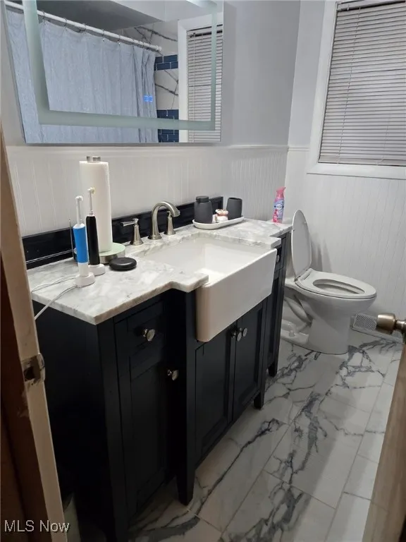 Full bathroom with vanity, marble finish floor, wainscoting, toilet, and a shower with curtain