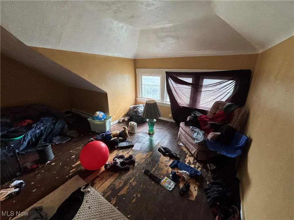 Additional living space with a textured ceiling, vaulted ceiling, baseboards, a textured wall, and hardwood / wood-style floors