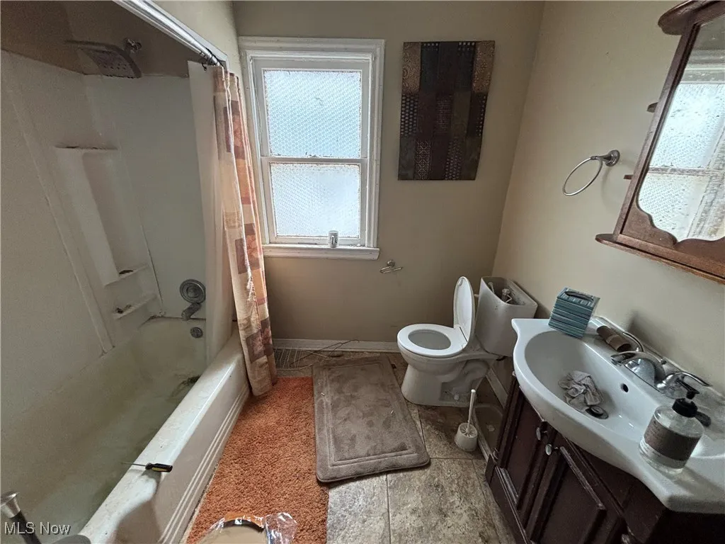 Bathroom with vanity, baseboards, shower / bath combo, and toilet
