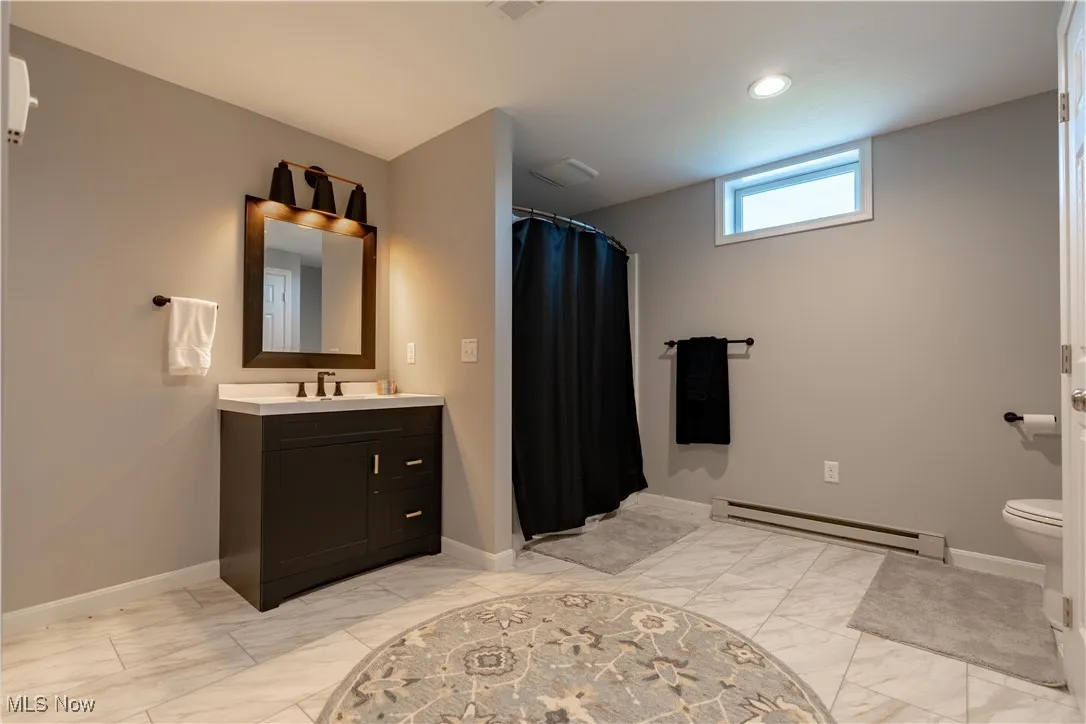Full bathroom featuring baseboards, marble finish floor, and a baseboard radiator
