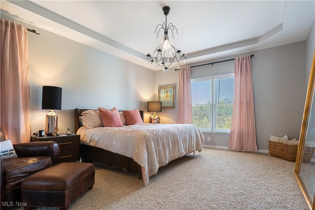 Bedroom featuring baseboards, a notable chandelier, carpet flooring, and a tray ceiling